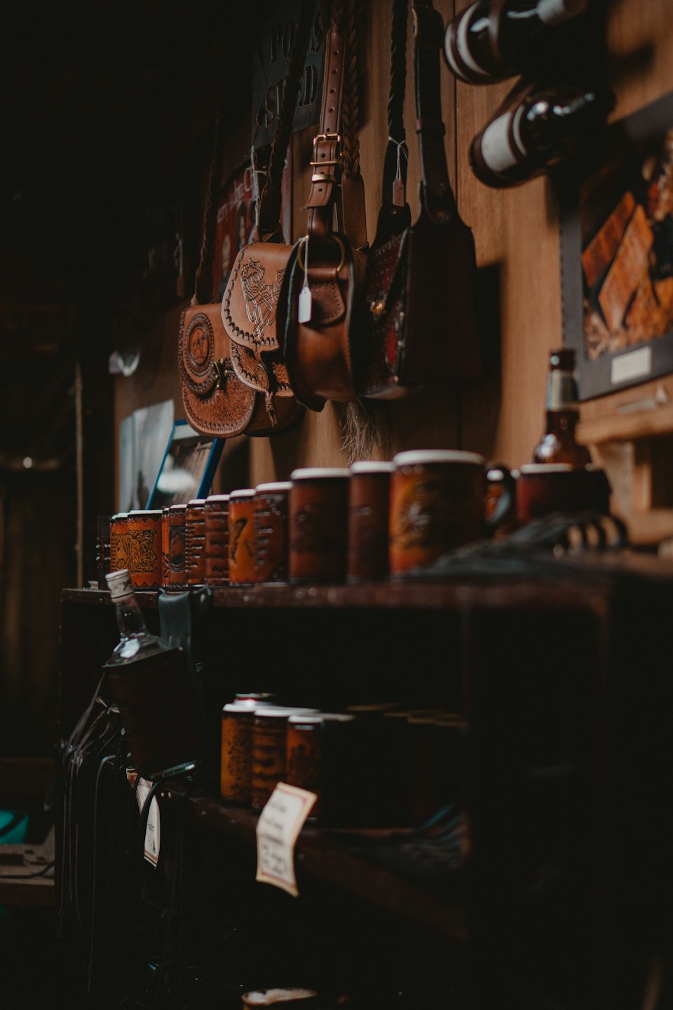Bolsos y tazas de cuero hechos a mano en una estantería de madera.