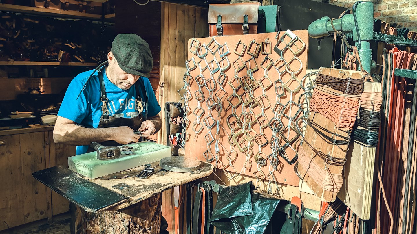 Artesano trabajando en hebilla de metal con herramienta pequeña.